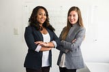 Two women in business attire, posing with arms crossed and smiling