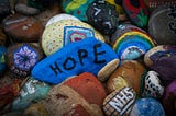 An artistic arrangement of painted rocks. The center rock features HOPE in large letters.