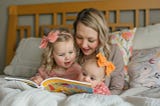 A mother reading to her two small children in bed.