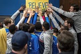 Soccer team from Ted Lasso touching a yellow sign that says BELIEVE