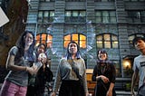 Half a dozen viewers look at a reflection of a spherical video installation projected on glass. The central most viewer’s head is nicely framed inside the spherical projection.