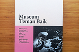 Buku Museum Teman Baik difoto di atas permukaan kayu yang datar. Sampul buku berwarna putih-merah muda di bagian atas bertuliskan judul buku, dan merah muda di bagian kiri bawah bertuliskan nama penulis serta editor. Terdapat foto hitam-putih dari beberapa hidangan.