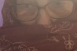 photo of the author’s head and shoulders, swathed in a dark burgundy scarf embroidered with large outlines of flowers in white thread, not for religious or cultural reasons, but because I’m cold.