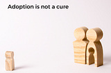 Text reads, “adoption is not a cure” and two wooden figurines are standing side to side. In one, there’s a hole in the shape of a small child. The child figurine is standing apart from the two ‘adults’.