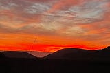 Bright orange sunset above soft curves of darkened hills