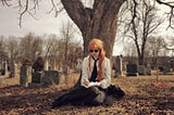 Holly Rhiannon with ginger hair dressed in a vintage style, writing in the Mont Royal graveyard.