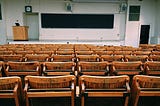 empty auditorium with wooden chairs, podium, and chalkboard