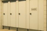 A row of bathroom stalls, with one labeled “KAORI.”