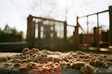 A heap of sand sits in a child’s playground, in front of a set of climbing bars which are out of focus in the background.