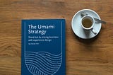 A book “The Umami Strategy” on a wooden tabletop with a white coffee cup next to it.