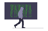 A person in a dark-grey hoodie,  walks — with their hands in their pockets — past a display of computer code on a very large screen. They might be glancing at the code as they pass.