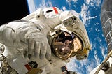 American astronaut space walks outside international space station with blue Earth in background.