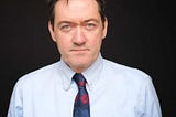 Image shows James Bullion, Chief Inspector of Adult Social Care and Integrated Care, CQC. James is against a black background, and is wearing a blue shirt with a blue and red tie.
