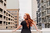 A redhead woman standing in front of a big city in san francisco