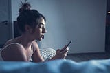 A woman holding a cell phone sexting with someone while looking depressed