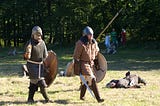 The explorer that stopped 5 minutes before the miracle. nicole wallet. two men dressed in Viking clothing carry shields and swords across a field, reincting a Viking battle.