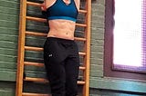 The author hangs by a bar with her head down and abs flexed, preparing to do a hanging leg raise