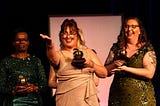 Danielle Hopkins smiles as she extends one arm and holds her Golden Apple award during a speech at the Golden Apple Teacher Recognition Banquet.