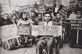 Black-and-white photograph of disabled World War II veterans in wheelchairs protesting on a New York City sidewalk, holding handmade signs reading ‘Don’t Let Us Down,’ ‘Keep Faith With Disabled Vets,’ and ‘Don’t Break Promises.
