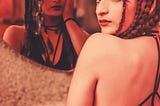 Girl sitting in front of a mirror that reflects a different version of her.