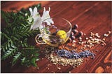 A transparent tea cup containing flowering tea. Lavender and condiments strewn around it along with a bunch of leaves.