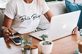 Should I start a blog — woman sitting at desk with a laptop and phone.