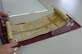 Ethiopian scroll being displayed on Wellcome’s custom-made scroll holder, made of clear plastic. Two hands are unravelling the scroll.