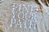 A dirt-washed T-Shirt with large, white block letters reading: “FIND YOUR PATH”