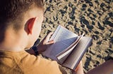 A man sits on the beach with an open book.