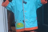 Picture of a happy three-year-old boy smiling in a blue and orange raincoat.