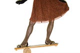 Woman dressed in cocktail dress, dress shoes, and black gloves balances with one foot on each end of a balance board.