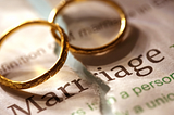 Two wedding rings on top of a dictionary definition of marriage.