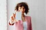 A young lady, blurred into the background, holds out a business card.
