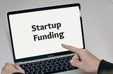 Finger pointing at laptop screen that reads “Startup Funding”