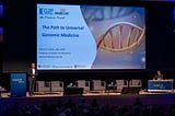 Dr. Robert C. Green stands at a podium in front of a screen displaying a title slide: “The Path to Universal Genomic Medicine.”