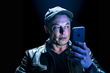MidJourney created image of Elon Musk in shadows looking at an iPhone held before his face. His face is lit by the iPhone.