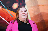 Writer Aubrey Gordon smiles in a photo wearing a black t-shirt and bright pink jacket.