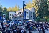 UCSC students gather at a rally for Rafah outside of the Palestine solidarity encampment on May 8. A university building, redwoods, and a blue sky are in the background. A banner on a lamp post in the foreground reads “Social Justice, The Real Change is Us.”