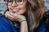 Young girl in a blue shirt, wearing glasses, smiling