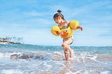 Young girl splashing in the ocean wearing a floatie.