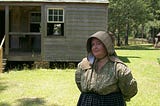 The writer in 1850s clothing in front of a farmhouse.