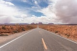 Photo of highway stretching off into the distance in the desert. Off in the horizon are jagged rocks and buttes. Scene where Forrest Gump running scene concluded