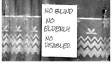 Black & white dated image from the 70’s of a poster in a window stating No Blind, No Elderly, No Disabled