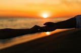 Silhouetted couple holding hands at sunset on the beach, symbolizing emotional connection and later-in-life love.