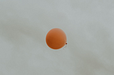 Orange balloon flying free in a grey sky.