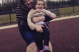 A mom and a little girl on a swing; wood chips on the ground