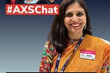 A woman named Shruti Pushkarna is smiling and wearing a colorful sari. She is wearing a name badge that reads “Disability” with a title under it. In the background, there are three individuals with a banner that says “#AXSChat.” The individuals are a man wearing sunglasses, a woman with purple hair, and another man wearing glasses.