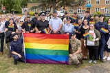 Group shot of MDP officers and staff standing with RAF Wyton personnel holding a rainbow flag, with buildings and trees in the background