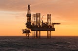 @SurferToday.com] [Toil’n’Trouble Alt-text: A photo of an offshore oilrig sits alone in high waters while the sky forms an orange sunset.]