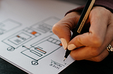 a woman writing notes on a ux wireframe drawing